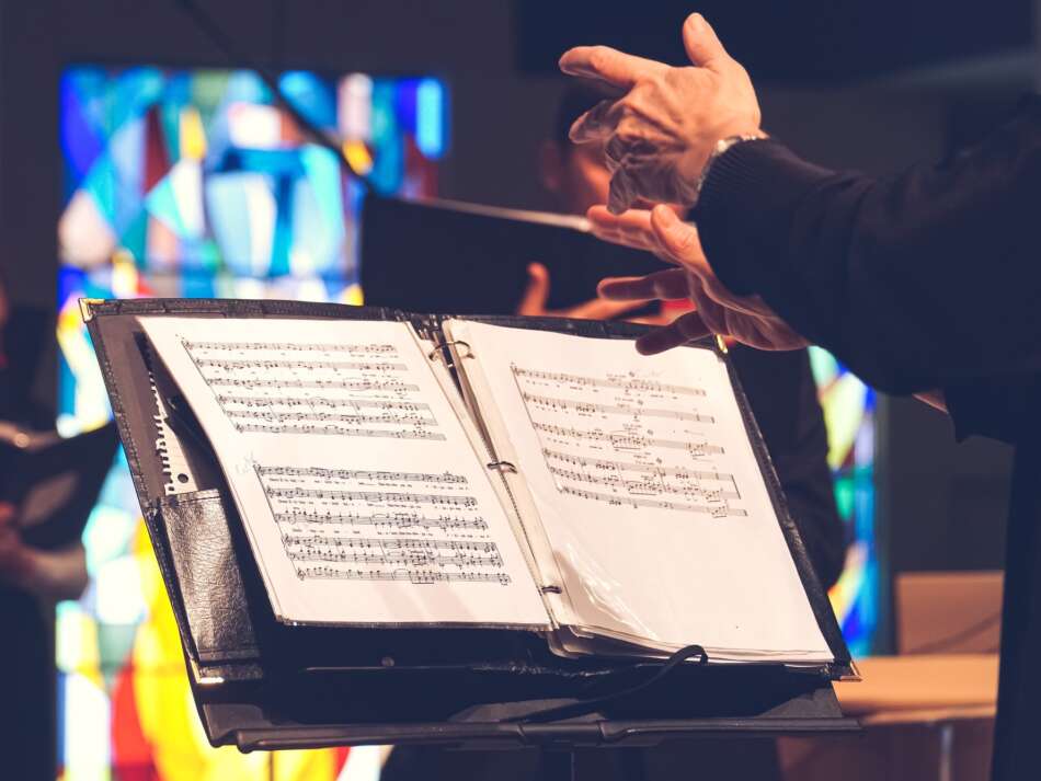 A conductor’s hands above sheet music sitting on a music stand