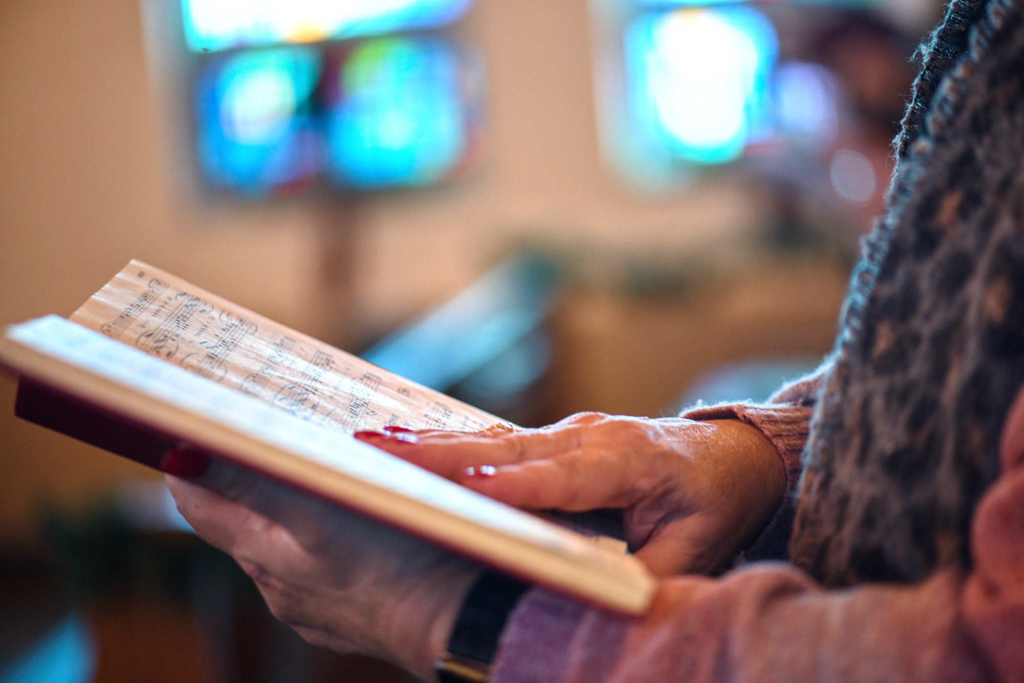 Unrecognizable middle aged baby boomer woman singing in church holding a music hymn book